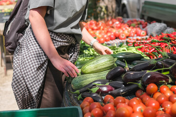 Young woman choosing fresh organic vegetables at a local market. Concept of eco lifestyle, sustainable food, mindful consumption, zero waste, farm produce, and conscious living.