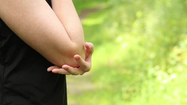 Elbow problem during training. Girl in sportswear massaging her bruised arm. Exercises in the forest. The athlete holds her hand after a possible sports injury. Pain in the elbow