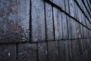 close-up view of blackened wooden shingles on an exterior wall; texture shows a burnt wood surface; Japanese technique "shou sugi ban" or yakisugi, commonly used in modern, eco-friendly architecture