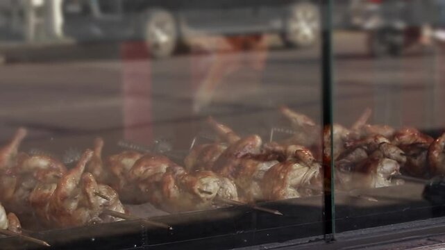 Rows of lechon manok or roasted chicken turning in the grill with the street view reflected on the glass display, showing authentic Philippine food culture and small business livelihood