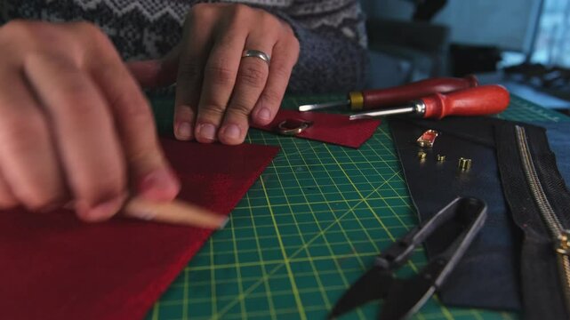 Leather craftsman smoothing red leather with wooden slicker on workbench