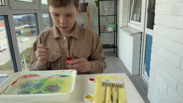 On the table, a boy is busy drawing Ebru, using a set of tools that support his artistic development and creativity.concept