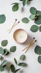 Flat lay of white ceramic candle with eucalyptus leaves and wooden matches on a white background

