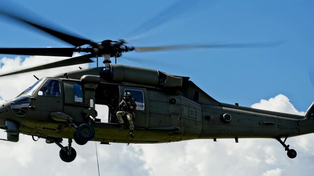 Military helicopter hovering in sky with soldier rappelling from it. Special forces rope insertion training footage.