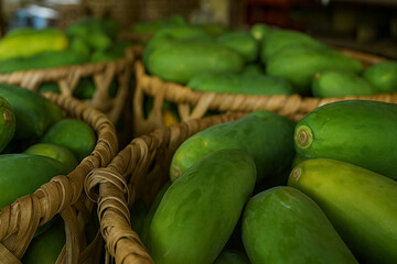 Green papayas displayed in traditional bamboo baskets at a local food market, highlighting freshness and natural produce.
