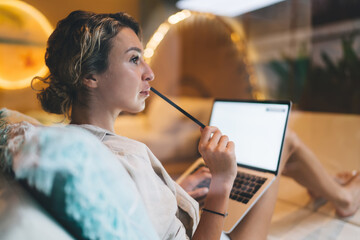 Woman typing on laptop with pencil in mouth, representing quirky approach to remote ideation,...