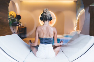 Headphones on, woman in meditation embraces digital serenity, facing window, disconnected from...