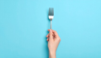 Close up photo of a hand holding a fork against a plain soft blue background