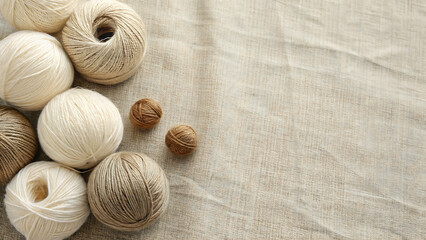 Cream and brown balls of yarn arranged on a beige linen fabric background