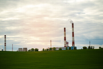 Industrial chimneys rising above green field at sunset, contrast between nature and industry