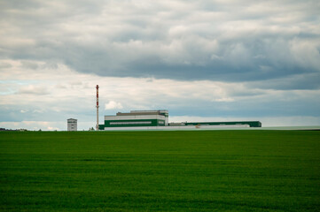 Factory complex by a wide green field under a cloudy sky, industrial meets natural landscape