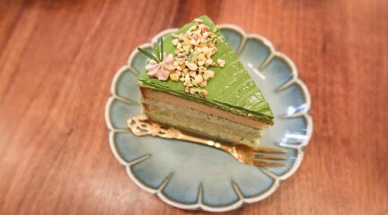 close up of a slice of green pistachio cream cake with layers on a floral plate with copy space on the wooden table 
