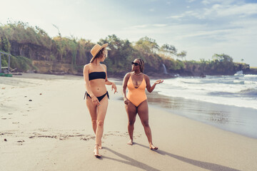 Two women walk barefoot on beach in relaxed conversation, reflecting authentic friendship, digital mindfulness and modern wellness through real-world connection, no devices visible.