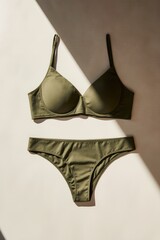 Olive green bra and underwear set on neutral surface, natural sunlight and soft shadows, minimalist, modern, stylish display.