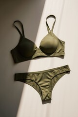 Olive green bra and underwear set on neutral surface, natural sunlight and soft shadows, minimalist, modern, stylish display.
