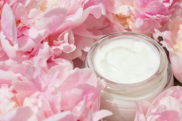 White Cream jar and peony flowers background. Cosmetic skincare product blank dark glass package. a bottle of unbranded lotion, balsam, hand creme mockup, flat lay