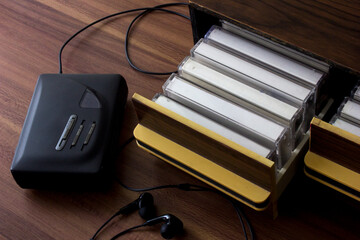 A portable cassette tape player on a wooden table. Next to it are several cassette tapes with blank white labels in a drawer.