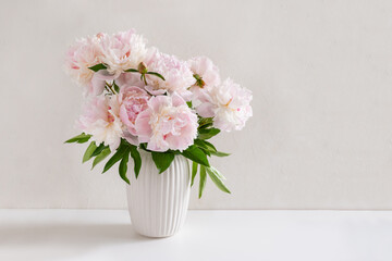 Bouquet of white and pink peonies in vase on pastel white background. Bright interior. Cottagecore Aesthetics. Floral composition. Greeting card. International Womens Day
