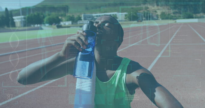 Fototapeta Drinking teenage athlete wearing green top with towel on red track, holding water bottle to mouth