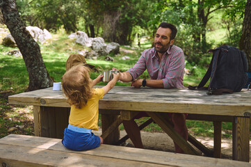 Father and Toddler Enjoying Quality Time at a Picnic Table in a Scenic Forest Setting