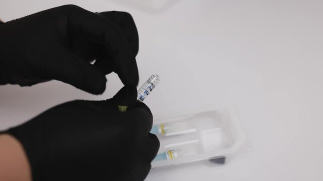 A professional cosmetologist wearing gloves prepares a syringe filled with a medicinal solution in a modern cosmetic clinic.