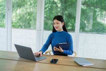 Young Asian female employee sitting and working in front of a laptop in an office.
