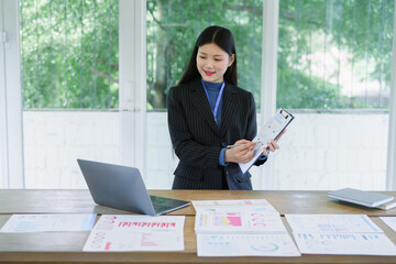 Freelance Asian woman writing in modern home office at night. Elegant young woman reading...