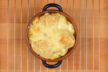 A top-down shot shows a baked cauliflower gratin with melted cheese in a brown oval dish with blue...