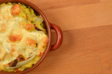 A top-down, close-up shot shows a brown oval baking dish with baked cauliflower gratin and melted...