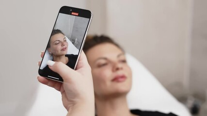 A cosmetologist takes a photo of a young woman's face on her phone after performing cosmetology services. The concept of distance learning and cosmetology services.