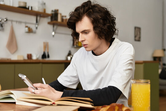 Young man enjoying a quiet morning at home while using his smartphone and sipping juice