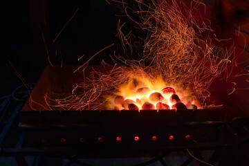 Sparks rise from burning coals in a mangal (grill, barbecue). Long exposure, dark night
