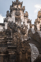 An ancient stone statue weathered by time, part of a majestic Balinese temple complex, under a soft sky