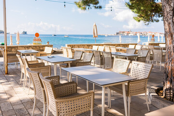Outdoor cafe with sea view and empty wicker chairs. Coastal relaxation, summer tourism, and beachfront dining in the Mediterranean region.