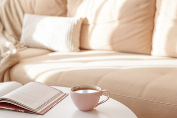 Cozy living room with a book and tea on a beige couch. Soft focus