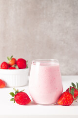Glass of fresh strawberry milkshake, smoothie and fresh strawberries on white and wooden...
