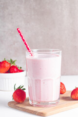 Glass of fresh strawberry milkshake, smoothie and fresh strawberries on white and wooden...