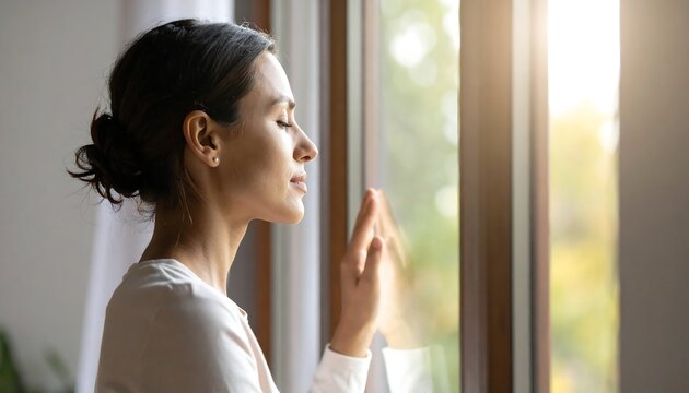 Woman meditating by window with sunlight.