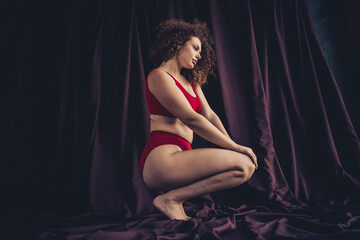 Young woman in red lingerie posing confidently against a draped purple textile background
