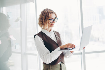 Successful businesswoman using laptop in modern office environment, executing professional tasks,...