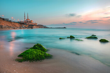 Long exposure photo of the beach with green rocks and light reflections.