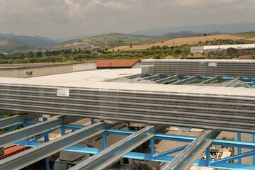 Sheet metal roofing on a steel structure under construction. Polyester sandwich panels. This image shows stacks of building materials on a metal roof of an industrial building.