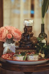 Traditional Thai Buddhist altar with Buddha statue, flower arrangement, and silver bowls