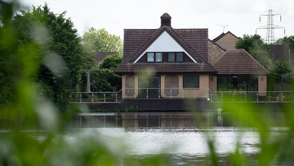 Detached house with triangular roof and wooden deck facing lake surrounded by lush green foliage