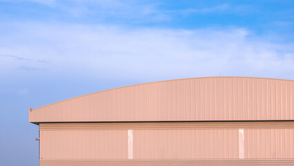 Large warehouse factory industrial building with dome roof and louver ventilation on aluminium corrugated metal wall against blue sky background, front view with copy space