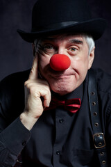 Dramatic portrait of a sad clown against a dark background.  Hand near face.