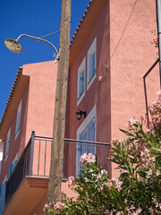Red-pink Mediterranean wall with blooming pink oleander in the foreground and a clear blue sky...