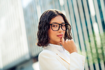 Fototapeta premium Confident businesswoman in glasses stands outdoors near a modern building, showcasing elegance and professionalism
