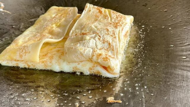 4k Street food vendor is preparing the dough and pan-frying paratha roti in hot oil until crispy on the outside. Street hawker preparing prata bread or roti canai for morning breakfast