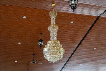 Luxurious crystal chandelier hanging elegantly from a modern wooden ceiling, complemented by...